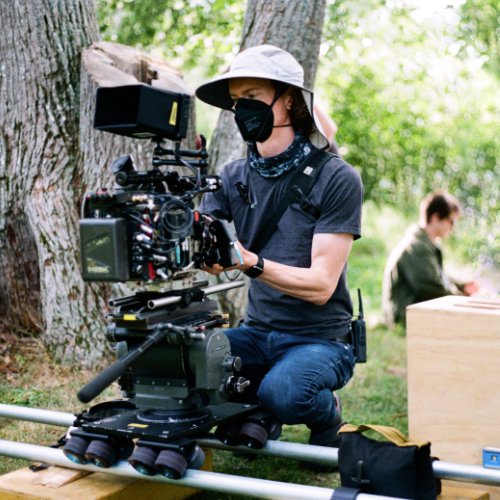 Ethan kneels to adjust the lens on a camera, which is mounted to a slider on the ground near a tree.
